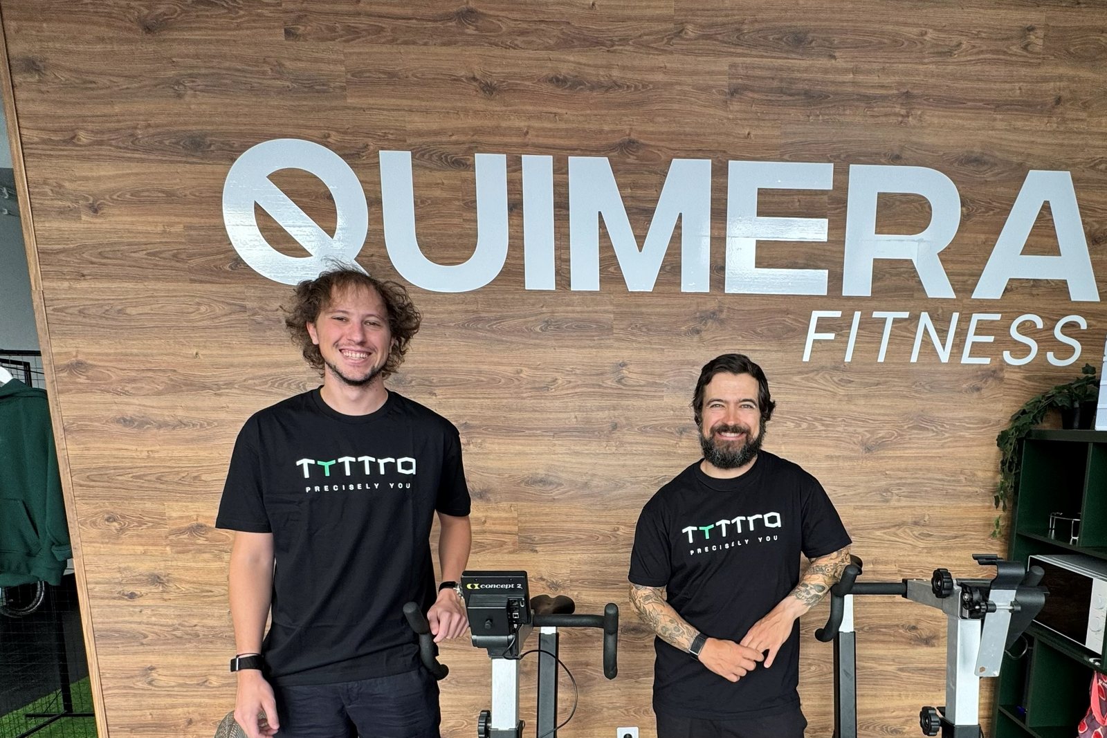Two people in Tyttra t-shirts at Quimera Fitness, in front of the gym logo